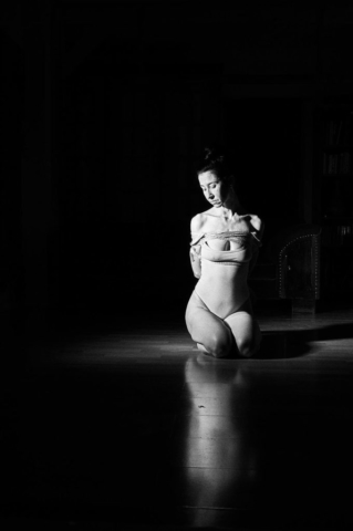 This picture depicts kinbaku photpgraphy in black and white film style. A beautiful woman with long black hair in rope bondage.