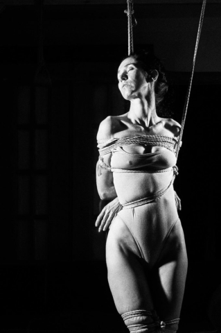 This picture depicts kinbaku photpgraphy in black and white film style. A beautiful woman with long black hair in rope bondage.