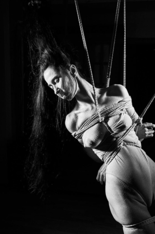 This picture depicts kinbaku photpgraphy in black and white film style. A beautiful woman with long black hair in rope bondage.